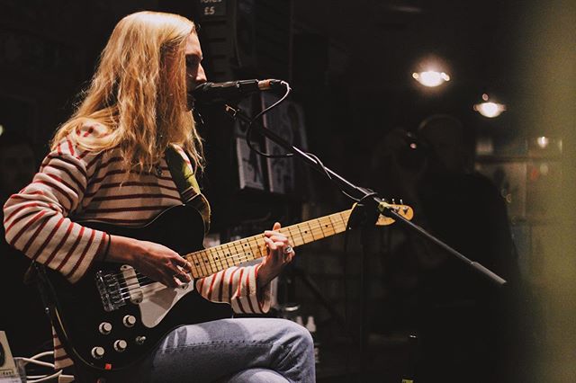 A woman plays electric guitar and sings into a microphone during a live music performance.