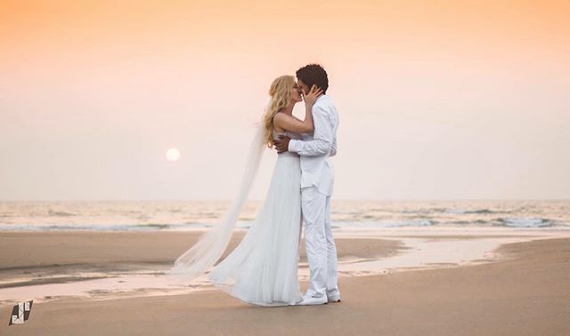 A bride and groom share a kiss on the beach at sunset, creating a romantic and intimate wedding moment.