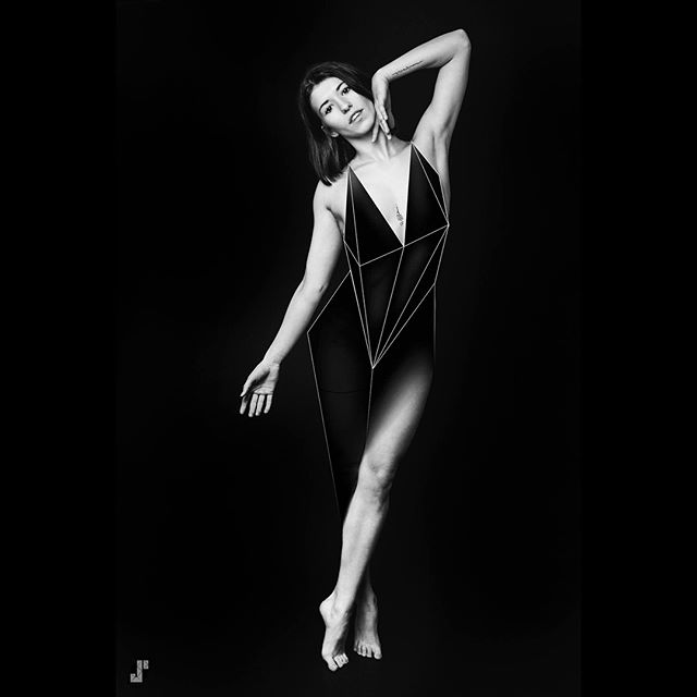 Artistic black and white image of a woman in a geometric-patterned bodysuit posing against a black background.