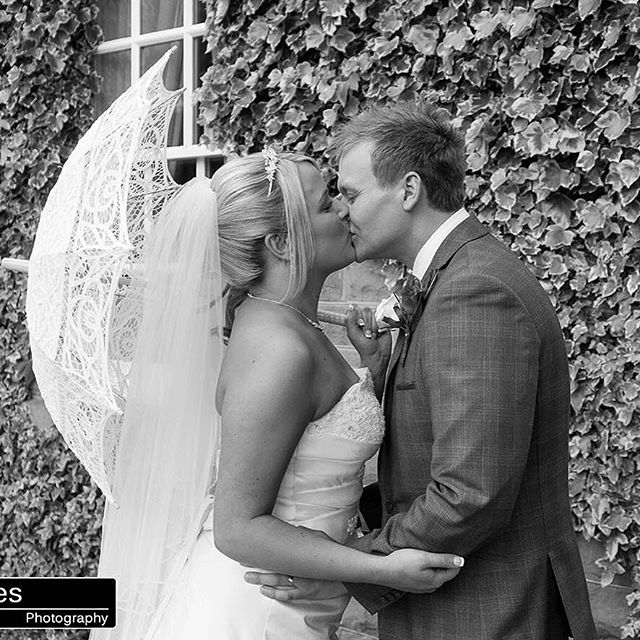 A bride and groom share a kiss in a timeless, romantic moment on their wedding day, captured in black and white.