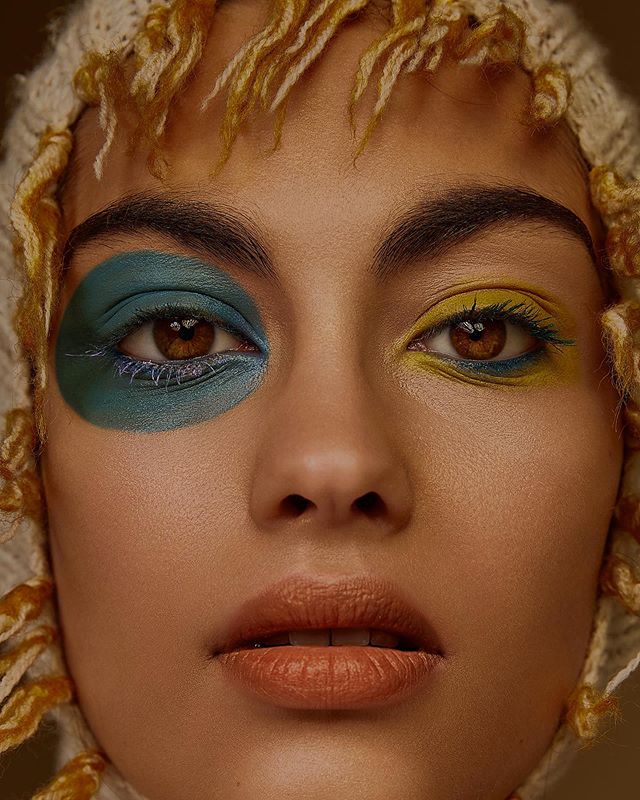 A close-up portrait of a woman with bold, colorful makeup, showcasing a modern editorial beauty style.