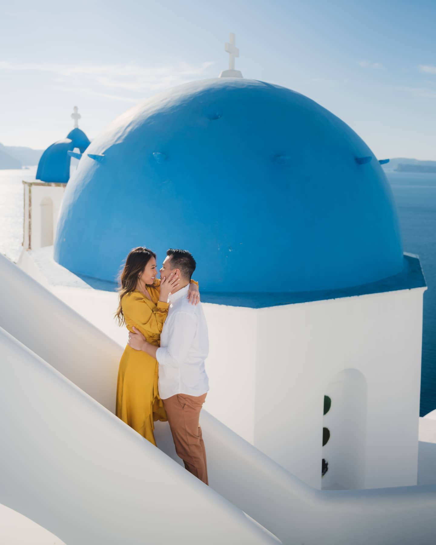 A couple embraces lovingly in front of a blue-domed church in Santorini, Greece, during their destination wedding.