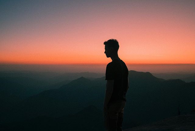 A silhouette of a man standing on a mountain, gazing out at a vibrant sunset.  