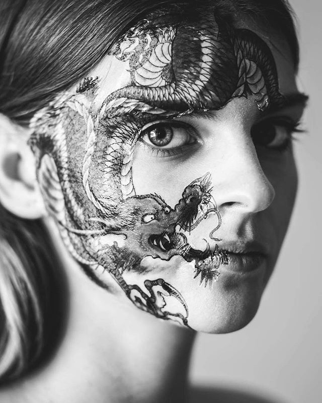 Artistic black and white portrait of a woman with a dragon face paint design.