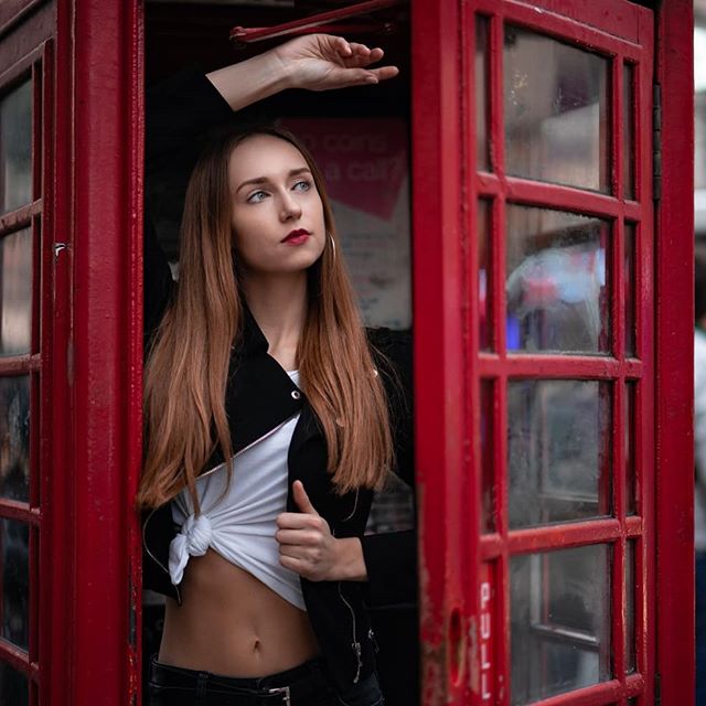 A stylish woman poses in a red telephone booth, blending urban fashion with classic London charm for travel inspiration.