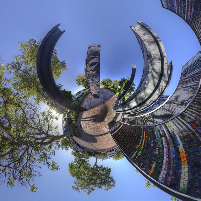 A vibrant, wide-angle view of a unique public art installation under a clear blue sky, set in a park. 