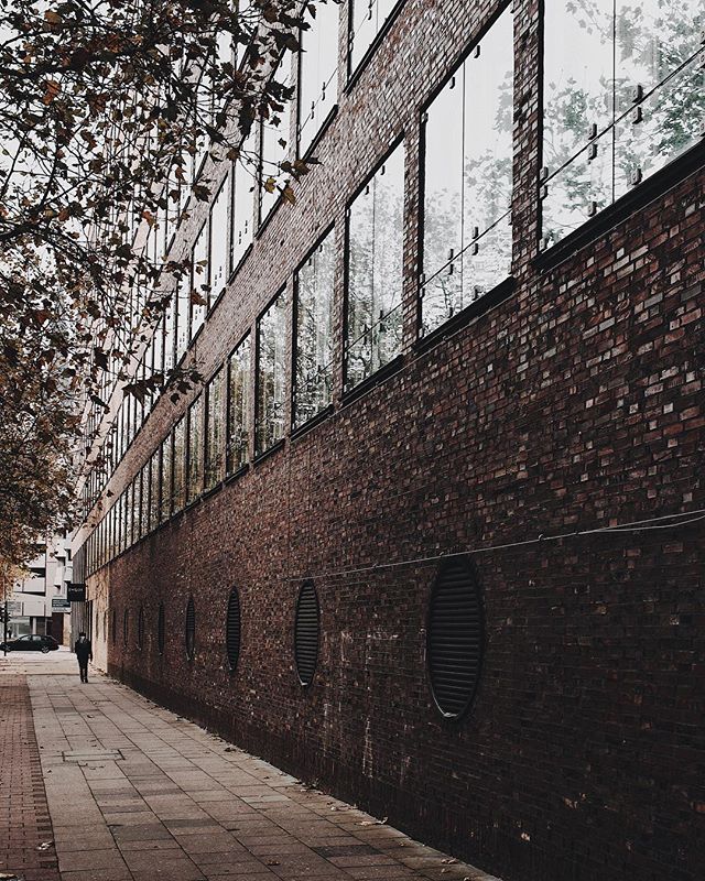 A person walks along a sidewalk next to a brick building with large windows in an urban setting.