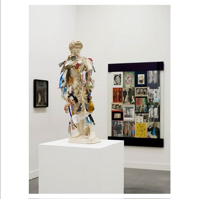 A modern art exhibit showcases a statue adorned with mixed media in a gallery, creating a thought-provoking visual.