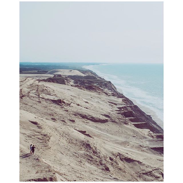 Scenic view of sand dunes meeting the sea, with a couple walking along the ridge.