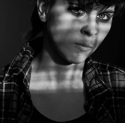 A black and white portrait of a woman with an intense gaze and moody expression in soft, artificial side lighting.