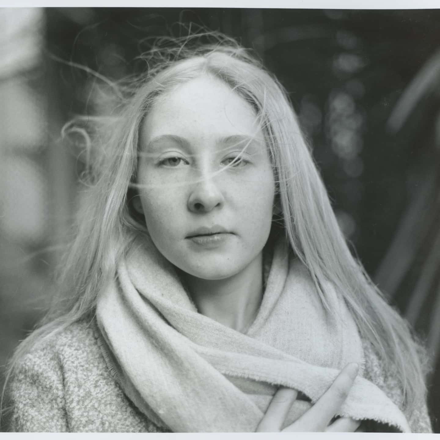 Black and white portrait of a blonde woman wearing a scarf, looking directly at the camera with a calm expression.