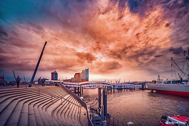 Hamburg's Elbphilharmonie concert hall and harbor viewed from the modern staircase with a vibrant sunset sky.