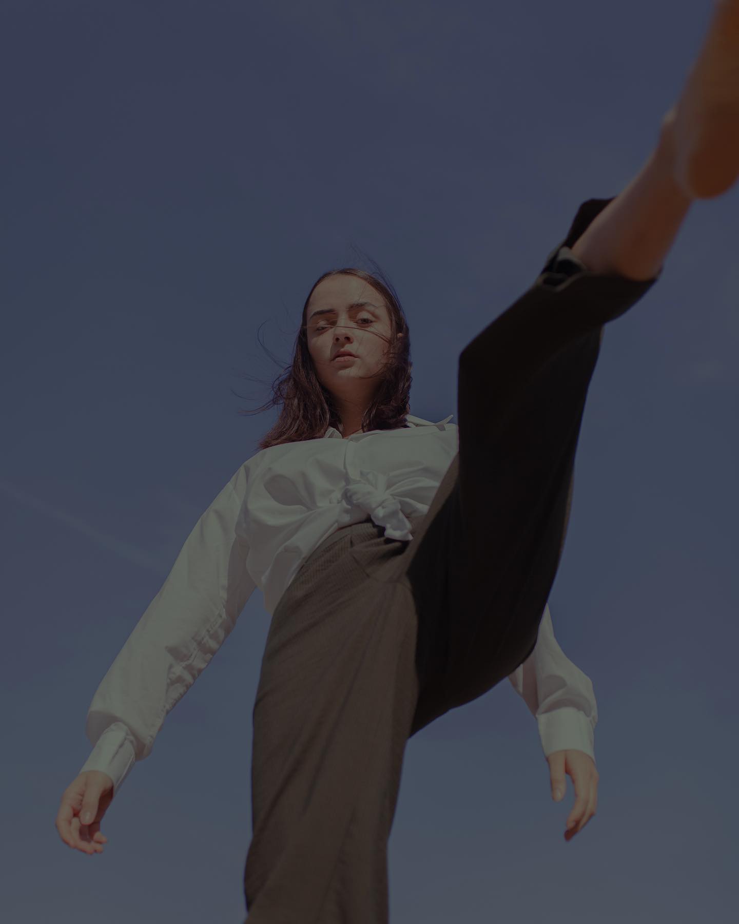 A woman poses confidently against a blue sky in a low-angle shot, capturing a moment of powerful self-expression.