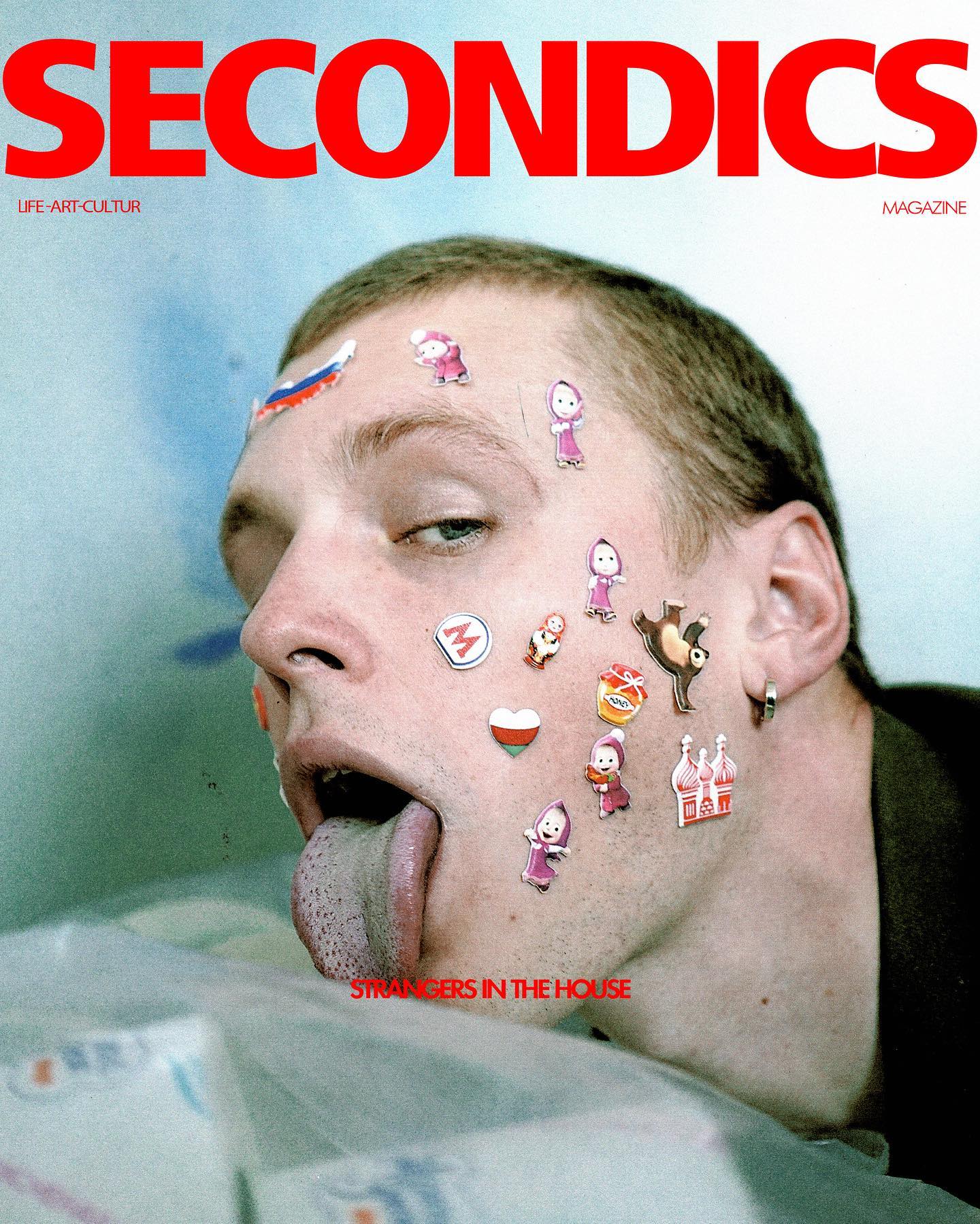 A man's face covered in stickers for a magazine, sticking out his tongue.