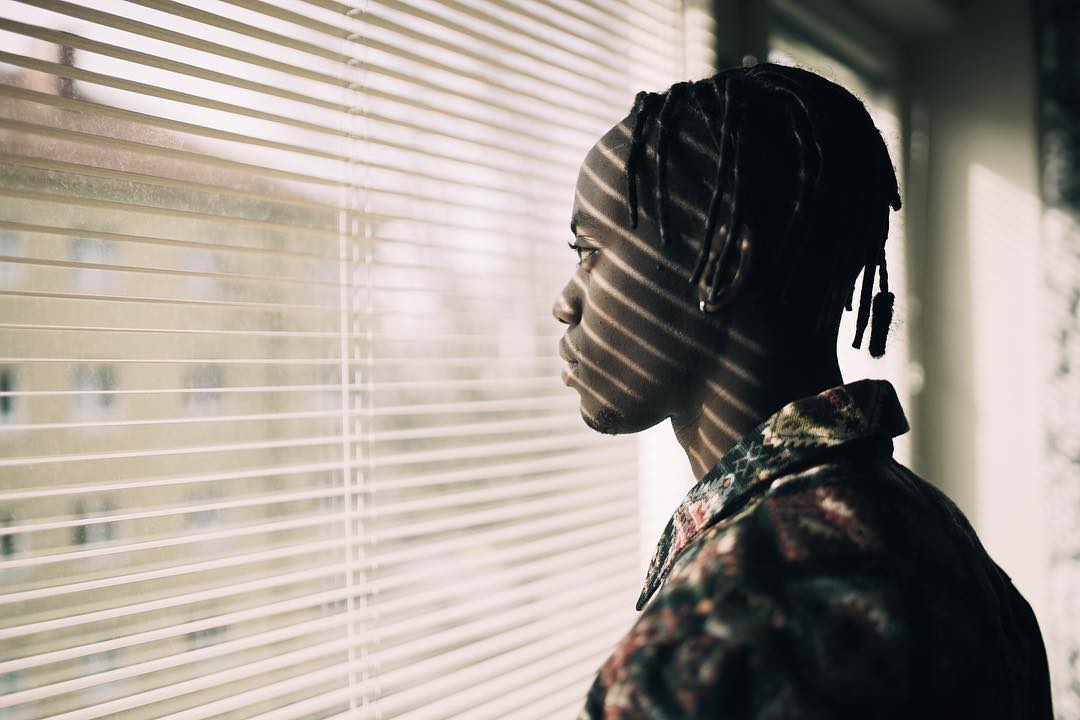 A man looks through window blinds, a thoughtful and pensive moment captured in an indoor setting.