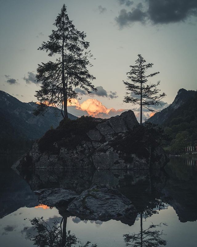 Tranquil scenery of Lake St. Sebastian, Austria, with trees on a rocky island reflected in the calm water at dusk.