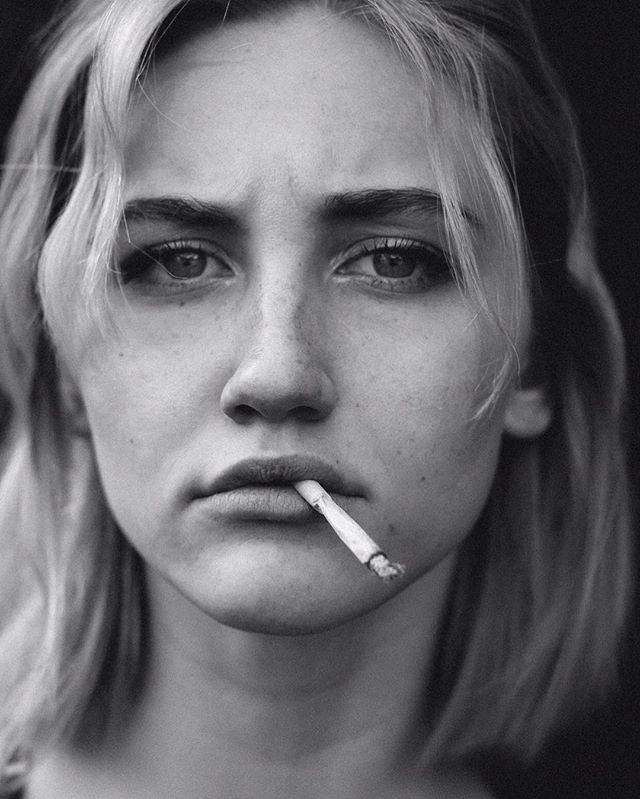 A striking black and white portrait of a woman with a cigarette in her mouth.