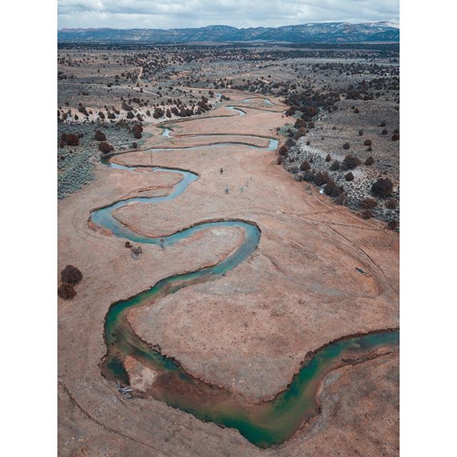 A winding river cuts through a dry landscape under a cloudy sky, showcasing nature's beauty from an aerial perspective.