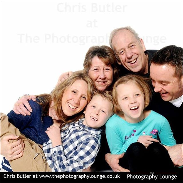 A multigenerational family gathers together for a cheerful portrait in a studio setting, showcasing warmth and connection.