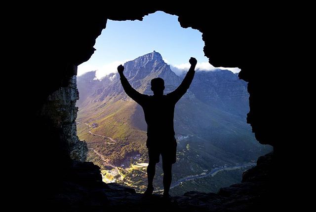 A silhouette of a man celebrating in a cave with a mountain view. Adventure and achievement concept.