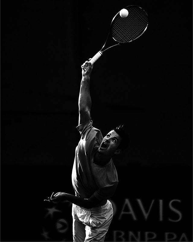 Monochrome action shot of a tennis player serving with intense focus and powerful form.