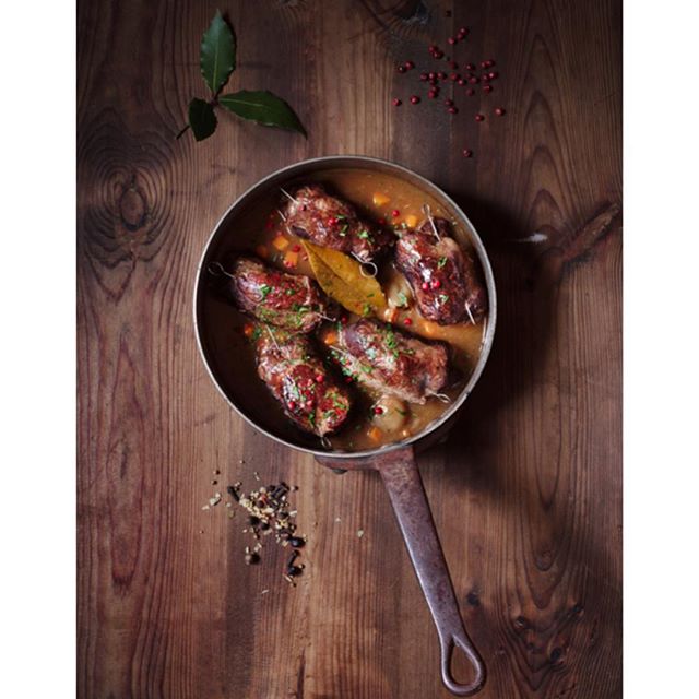 Overhead shot of rouladen in a pan with bay leaf on a wooden table, perfect for food and lifestyle content.