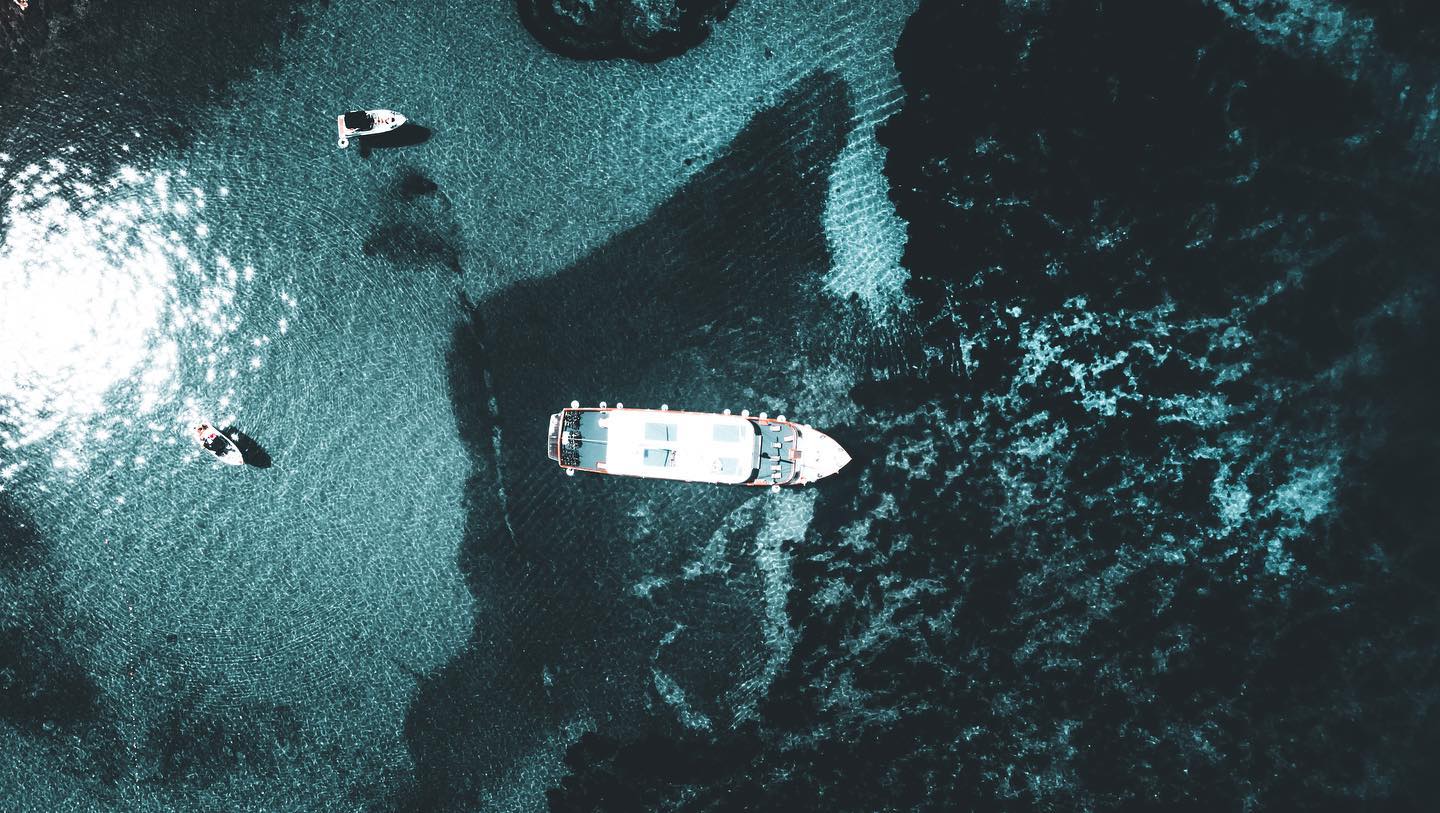 Aerial view of boats and yachts sailing on clear waters on a sunny day by the coast.