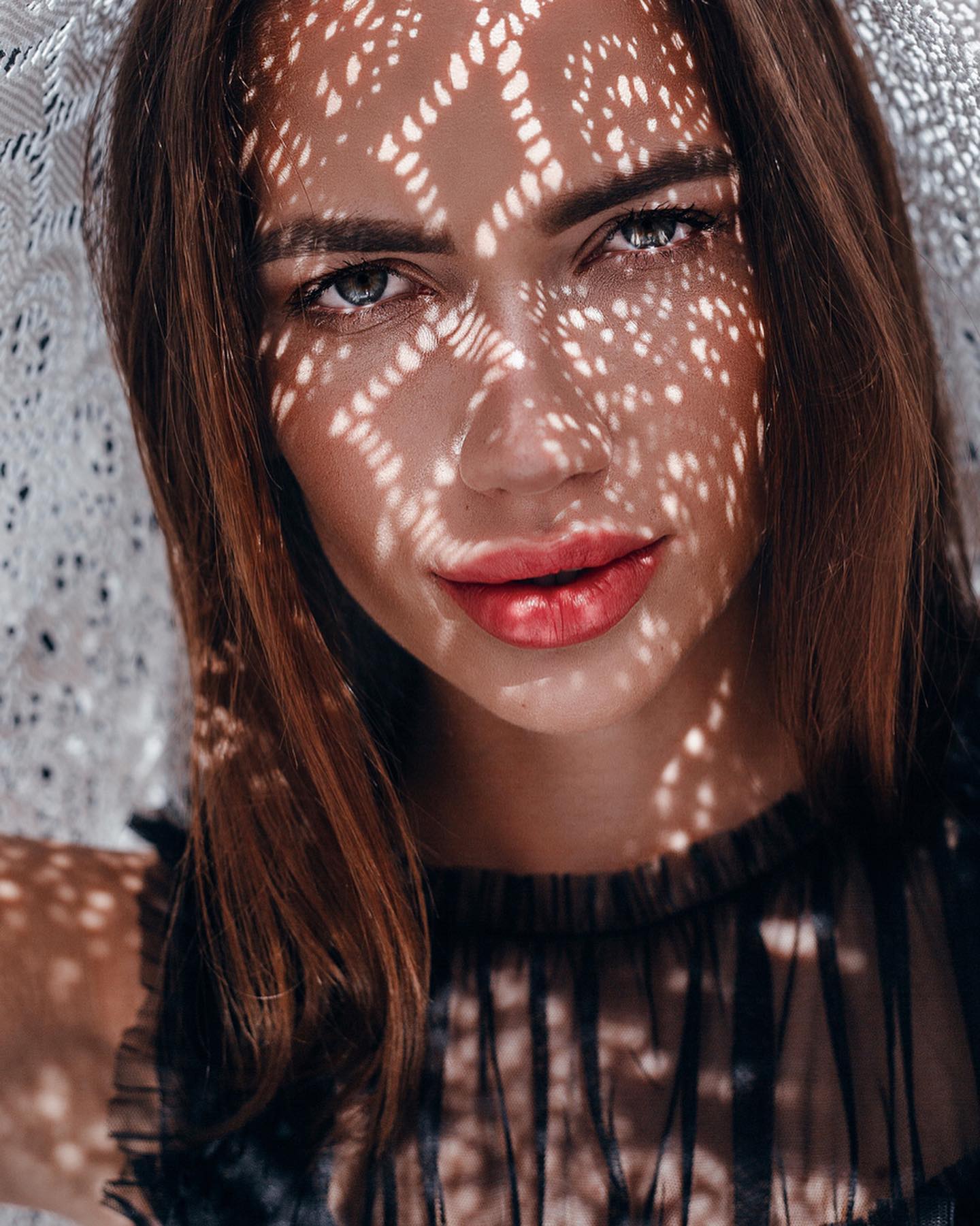 A beautiful woman with shadow patterns on her face under a lacy hat, creating a dreamy, sensual portrait.