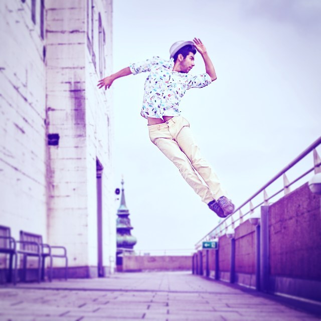 A man in a hat leaps against the city skyline in a dynamic, eye-catching pose.