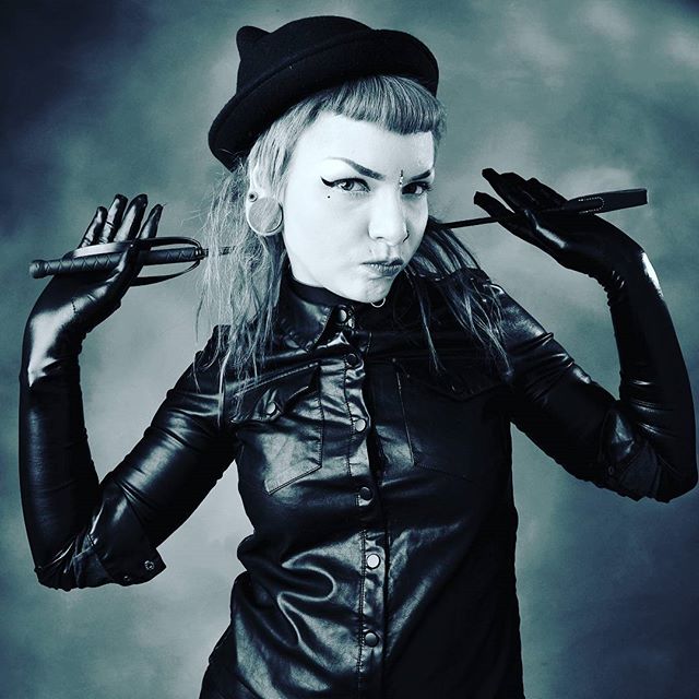 A woman in a hat and leather jacket poses with gloves on, exuding confidence and style.