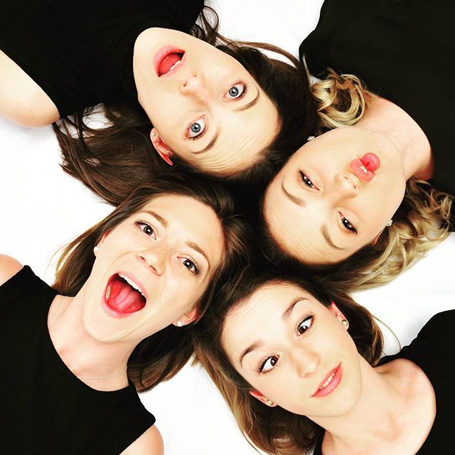 Four smiling women lying in a circle, creating a fun and engaging group portrait on a white background.