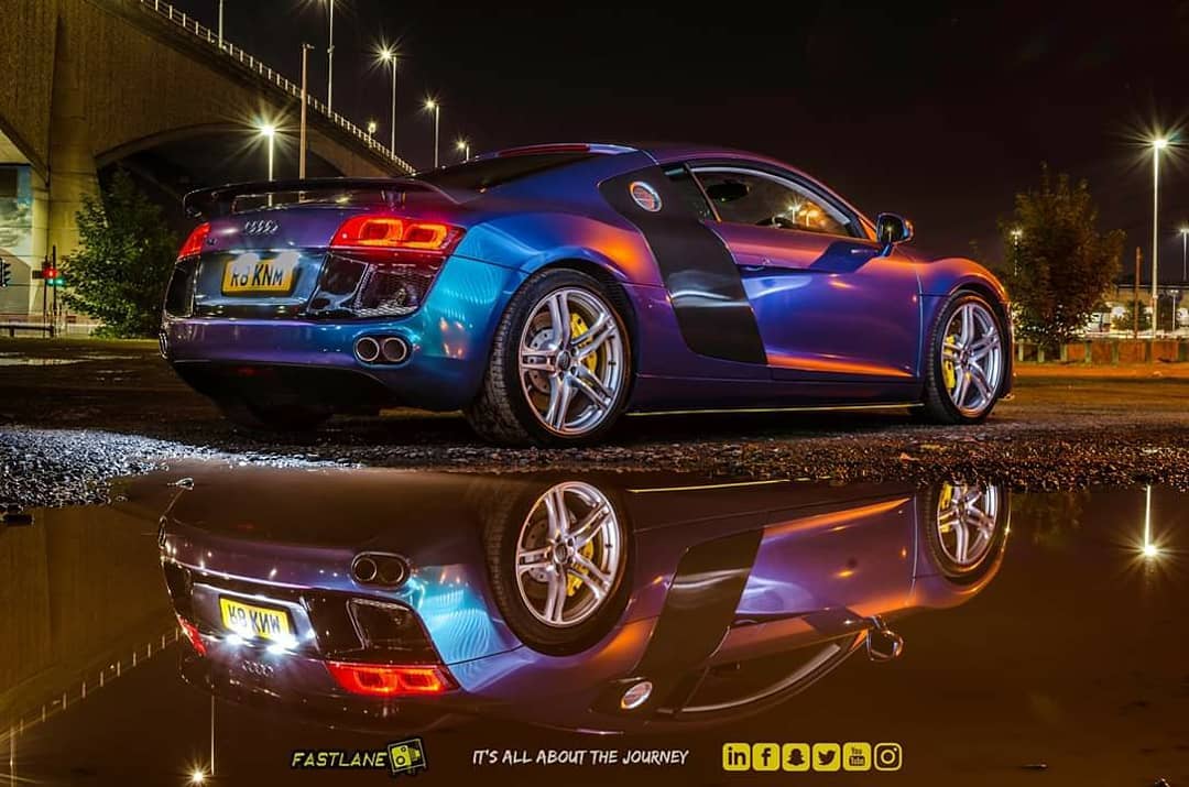 A vibrant Audi R8 sports car is reflected in a puddle at night, showcasing its sleek design and performance appeal.
