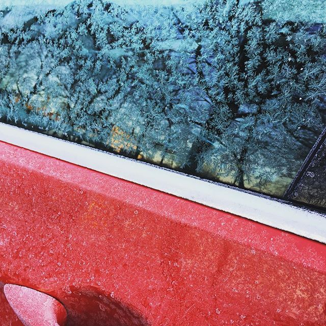 Frost crystals form intricate patterns on a car window in this close-up winter scene.