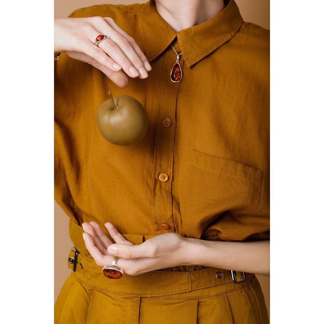 A woman in gold clothing showcases jewelry and an apple in a studio setting.
