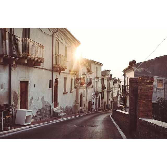 A quiet street winds through an old European town, bathed in warm sunlight. The scene evokes tranquility and timeless charm.