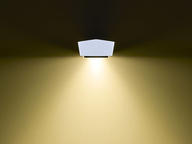 Modern white wall lamp illuminating a wall with a soft, warm glow, creating a serene and harmonious atmosphere.