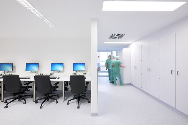 Bright hospital office space with doctors in scrubs and computer workstations.