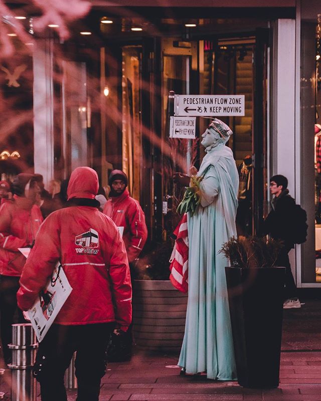 A street performer dressed as the Statue of Liberty entertains pedestrians on a vibrant city street at night.