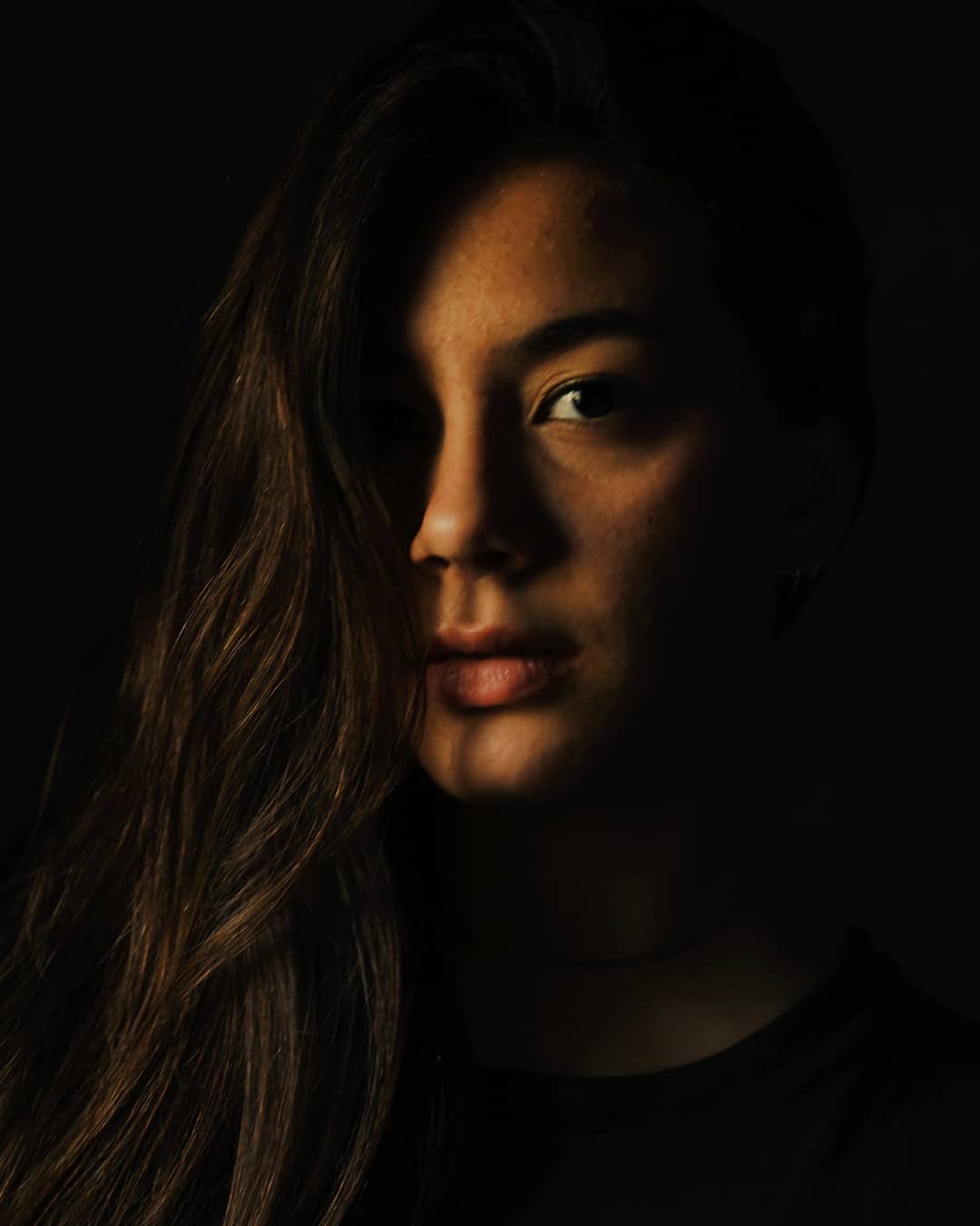 A striking portrait of a woman in shadow with soft light, creating an intense, moody atmosphere.