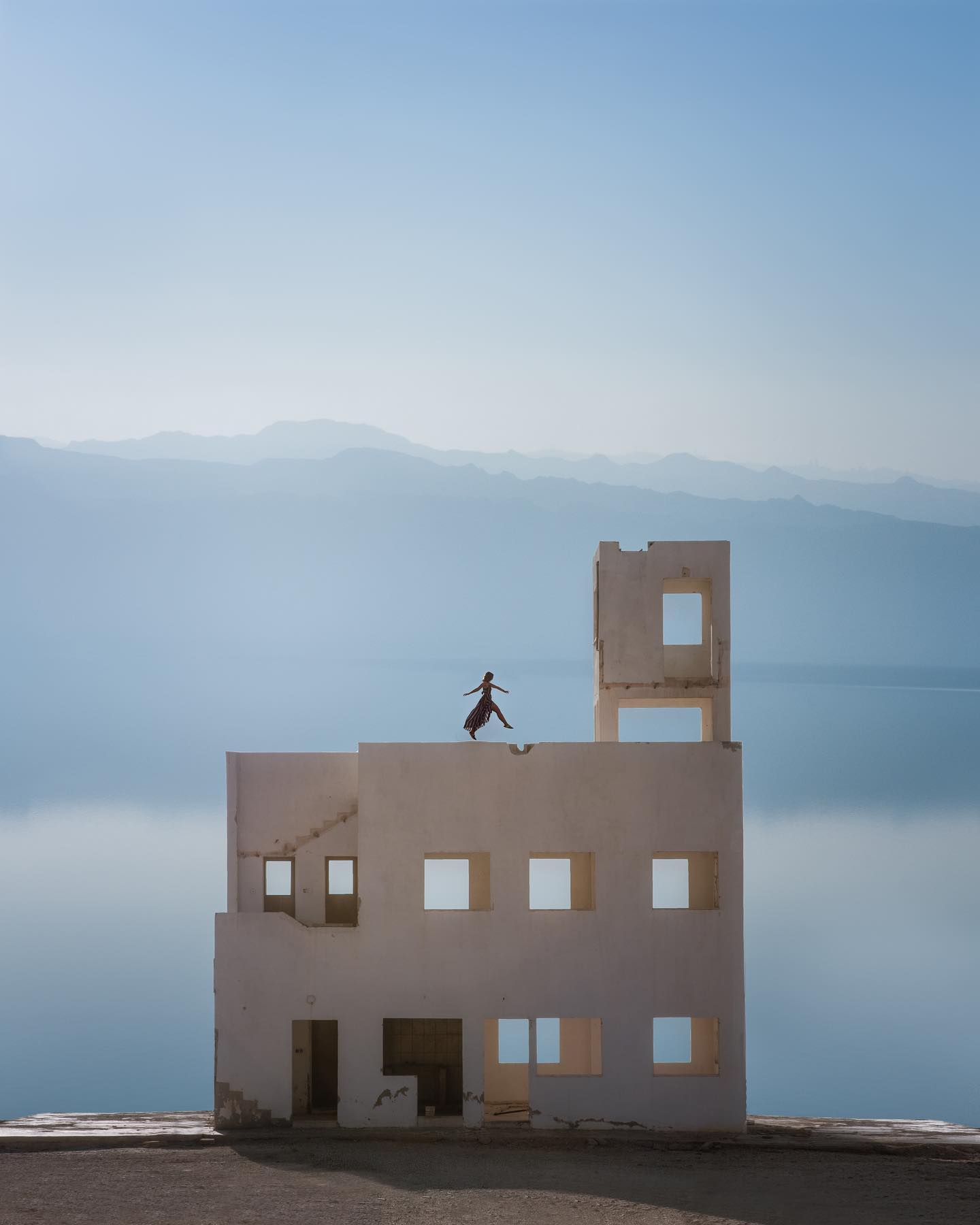 A woman stands atop an abandoned building overlooking the Dead Sea, capturing a sense of solitude and surreal beauty.