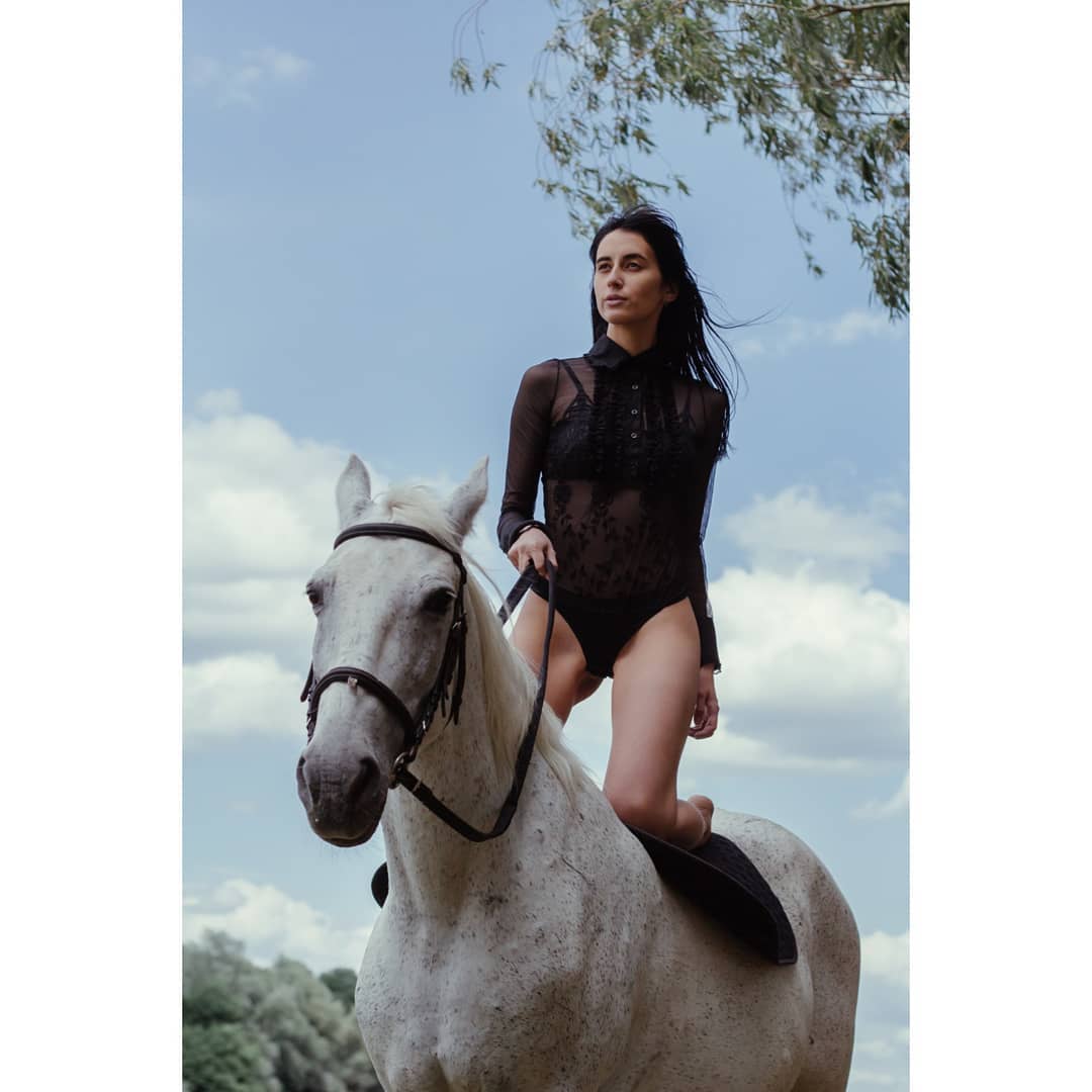 A confident woman rides a white horse in a sunlit field. Equestrian fashion and freedom.
