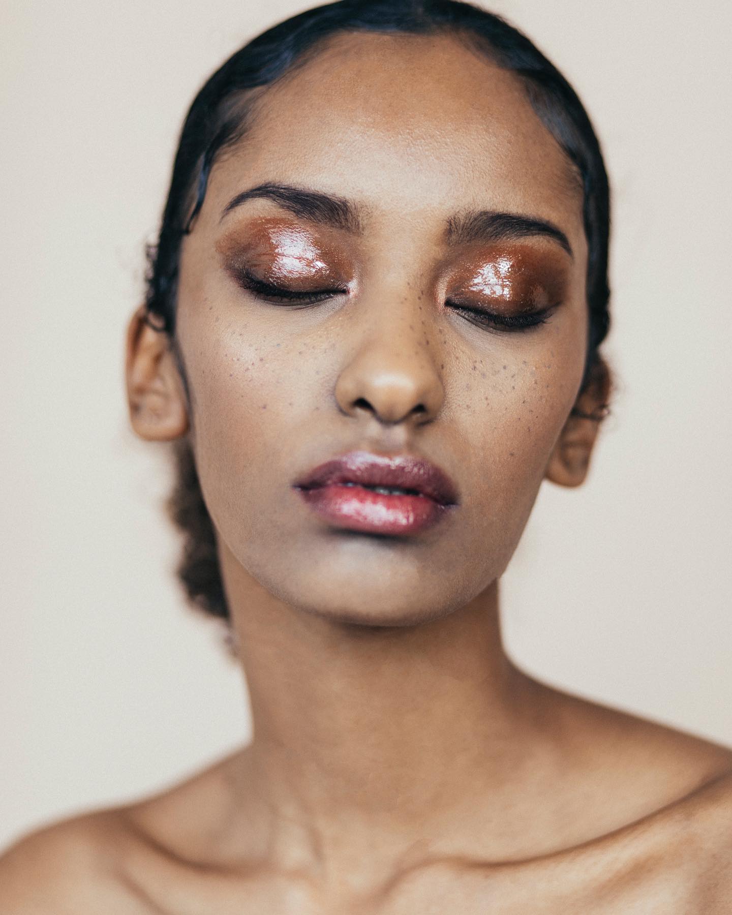 A woman with glossy eye makeup poses in a close-up portrait.