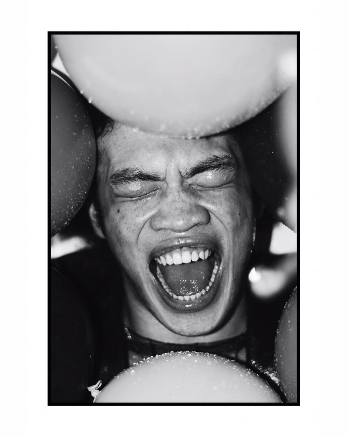 A close-up, black and white portrait of a man with balloons, expressing intense emotion.