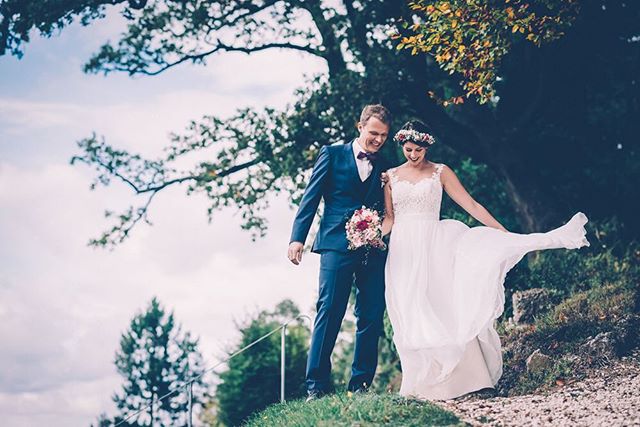 A bride and groom stroll down a hillside path on their wedding day, bathed in soft, natural light.