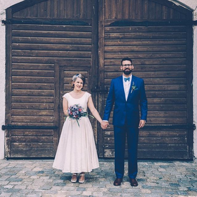 A happy bride and groom holding hands on their wedding day in front of a large wooden door.