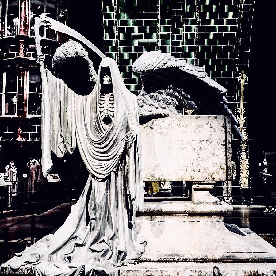 A statue of the grim reaper stands next to a tombstone, on display at a museum.