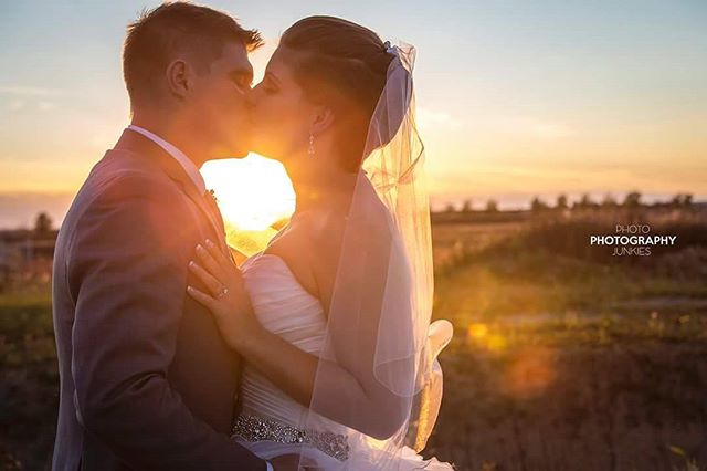 A bride and groom share a kiss during sunset on their wedding day in a picturesque outdoor setting.