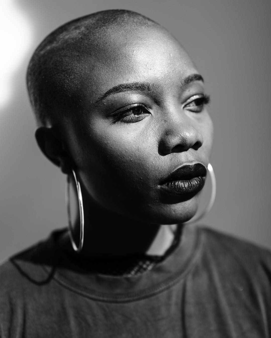 A striking black and white portrait of a bald woman with bold lipstick and hoop earrings, confidently gazing away.