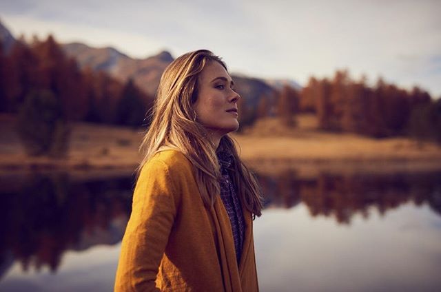 A woman in a cardigan stands by a lake, enjoying the autumn scenery.