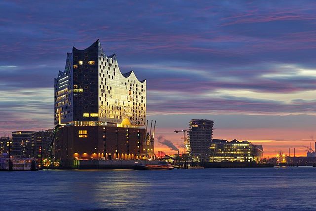 Illuminated Elbphilharmonie concert hall in Hamburg at dusk, reflecting on the Elbe river.